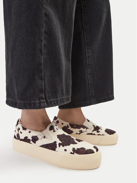 Person wearing black denim wide-leg pants and beige-soled cow-print slip-on sneakers.