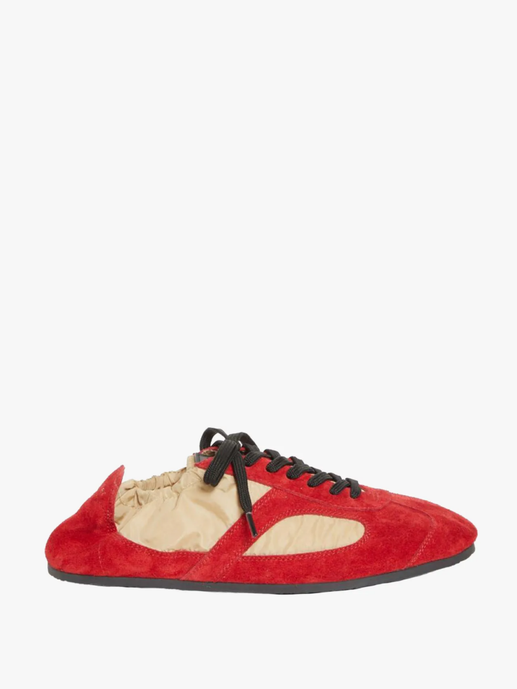 Red suede sneaker with beige fabric side panels, black laces, and a flat black sole.