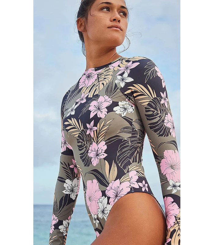 Woman in a long-sleeve floral swimsuit at the beach, with pink, white, and beige flowers on a dark background.