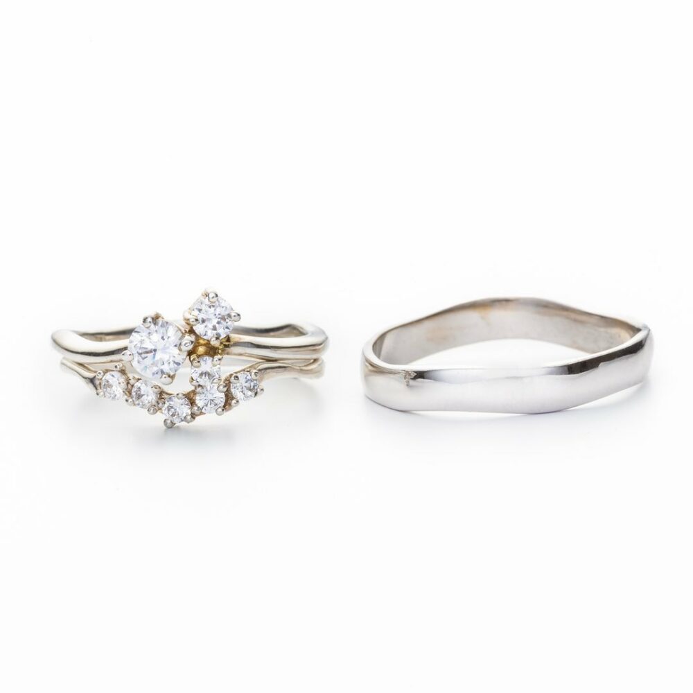 Two rings on a white background: a diamond cluster engagement ring beside a plain silver band.