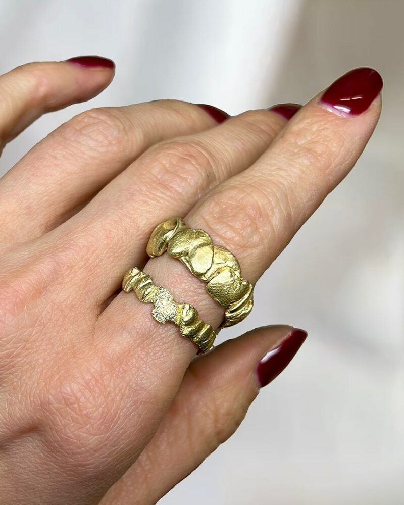 Close-up of two textured gold rings worn on a finger with red nail polish visible nearby