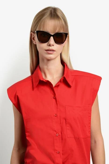 Woman with straight blonde hair wearing a red sleeveless button-down shirt and dark sunglasses against a light background.