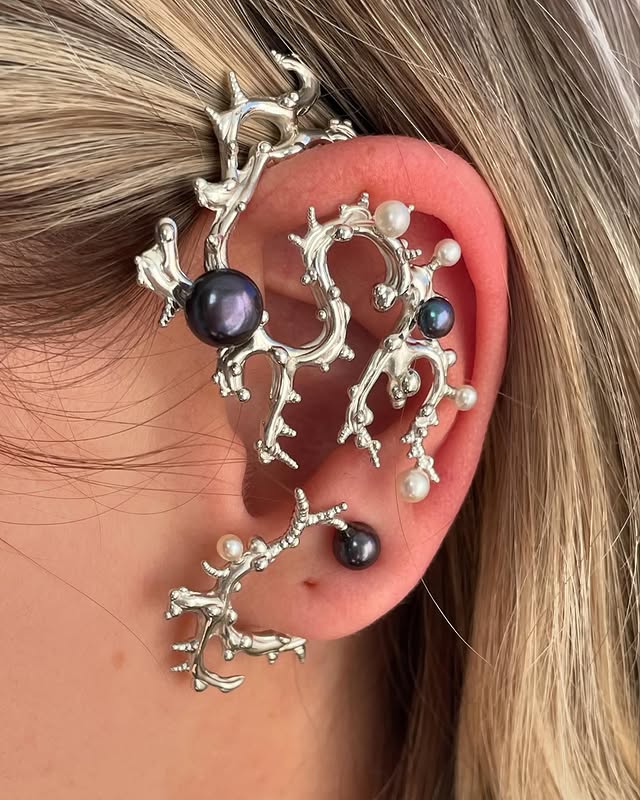Silver coral-shaped ear cuff with dark pearls and tiny white pearls wrapping along the ear’s outer edge, creating a dramatic statement jewelry piece.
