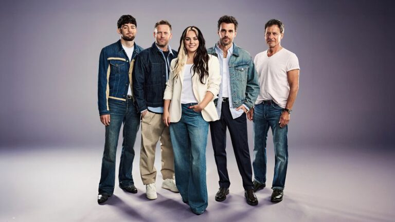 Five adults posing together in denim outfits in a studio, looking at the camera.