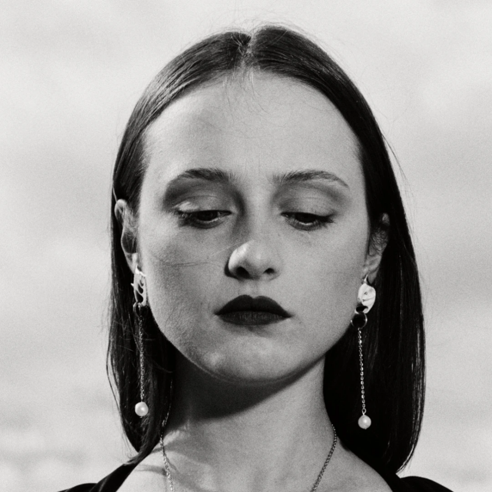 Black-and-white portrait of a woman with straight hair, dark lipstick, and long drop earrings.