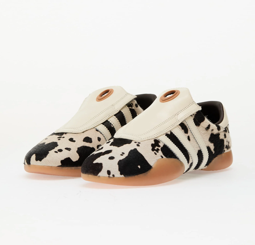 Pair of cow-print sneakers with cream uppers and tan rubber soles, photographed on a white background.