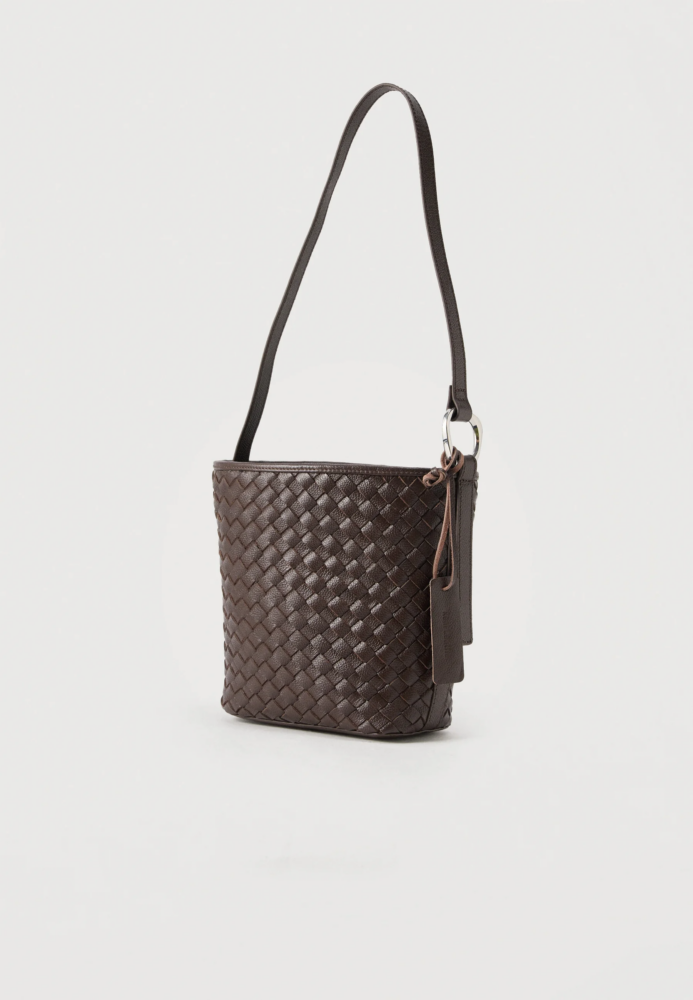 Brown woven leather handbag with a long strap hanging against a white background, showing textured pattern and metal ring detail.