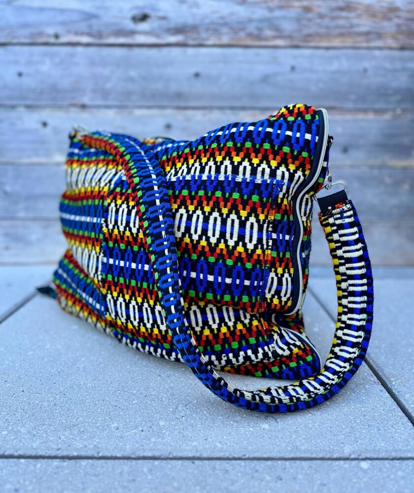 Colorful woven shoulder bag with blue, red, yellow, green and white patterns resting on a concrete surface.