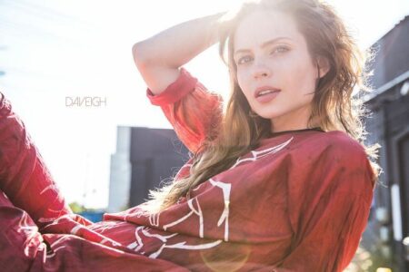 Woman in a red printed blouse posing outdoors, looking toward the camera with sunlight glare on her face.