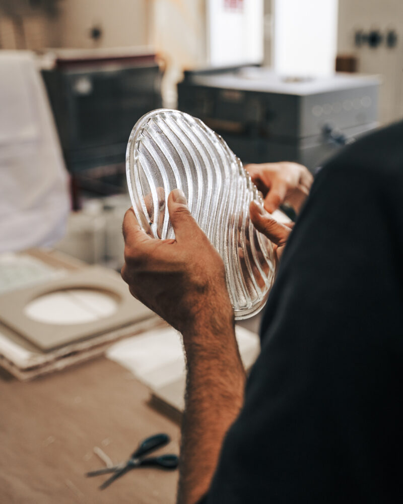 Person holds a round, ribbed aluminum pan in a workshop, with tools in the background, focusing on the pan's shiny surface.