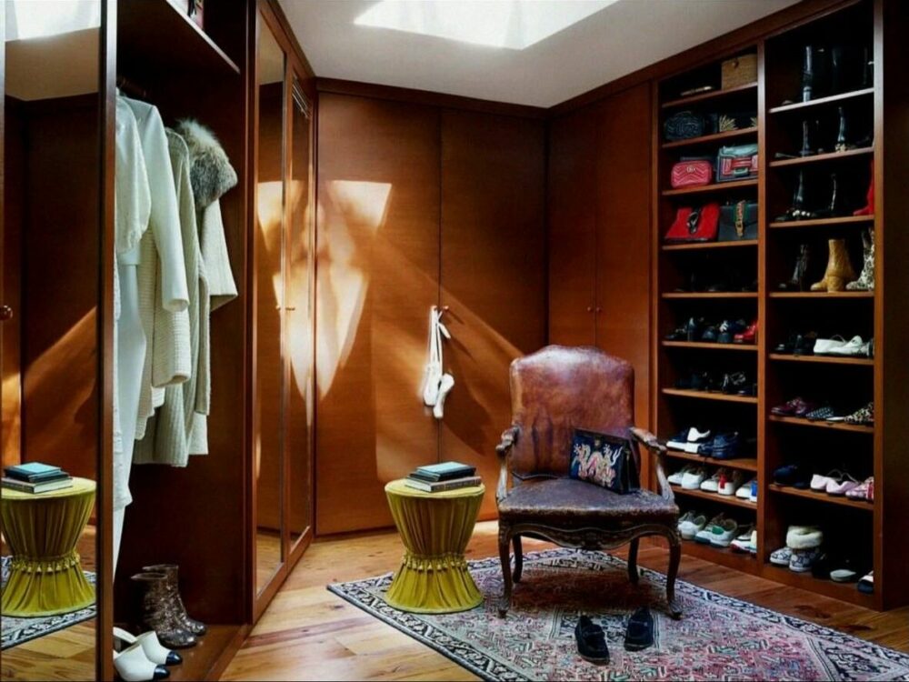 Walk‑in wooden closet with built‑in wardrobes, shelves full of shoes on the right, hanging robes on the left, and a vintage leather chair in the center.