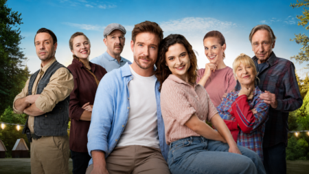 Eight adults posing outdoors, smiling, with a blue sky and trees in the background.