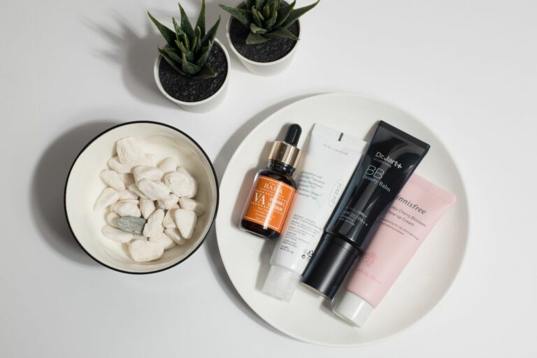 Flat lay of skincare products on a white round tray with a small bowl of white stones and two potted succulents nearby.