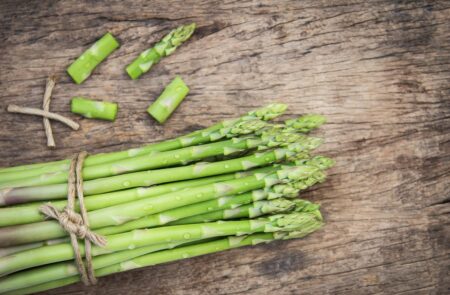 Bundle of fresh green asparagus tied with twine on a wooden surface, with a few tips separated nearby