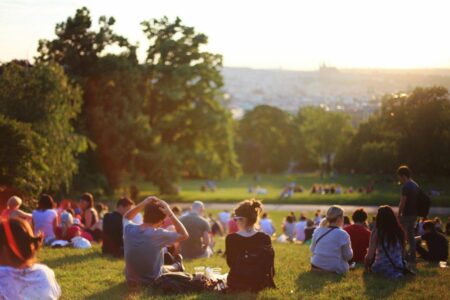 People picnicking on a grassy park hill at sunset, with a distant city skyline.