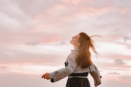 Woman standing outside at sunset with arms outstretched, smiling as her wind-blown hair flows in the breeze.
