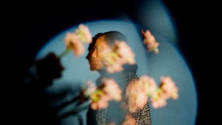 Side-profile portrait of a man inside a blue circular light, with blurred pink flowers in the foreground.