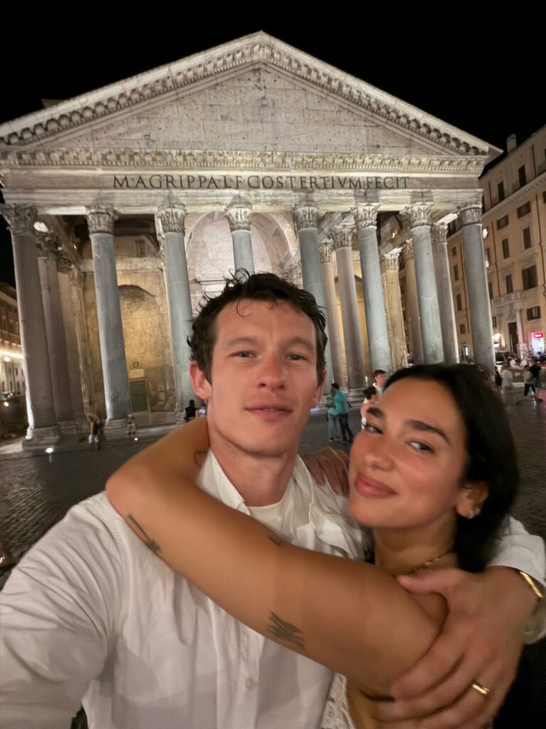 Couple taking a nighttime selfie in front of the Pantheon, arms around each other, with the temple's columns visible behind them.