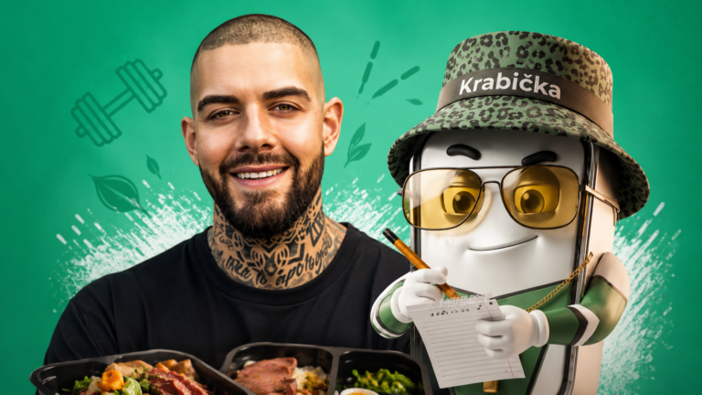 Smiling tattooed man beside a friendly robot in a leopard-print hat labeled 'Krabička', taking notes on a notepad with a pencil, bowls of food in front.