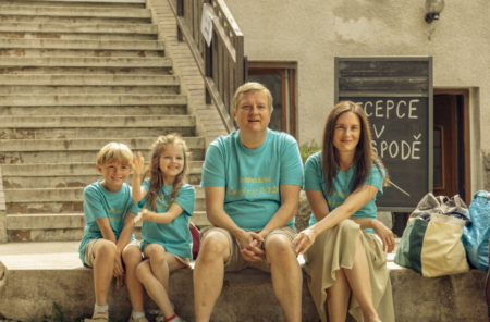 Family of four in teal T-shirts sits on outdoor stone steps, posing for a photo.