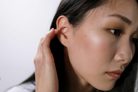 Close-up of a woman gently touching her ear with her right hand.