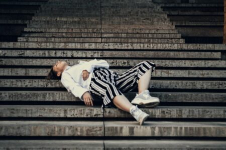 Person lying on concrete stairs, wearing a white shirt, black-and-white striped skirt, and sneakers.