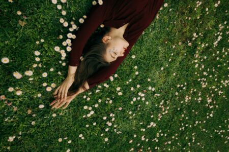 Woman lying on her side in a meadow of white daisies, wearing a burgundy dress, eyes closed.