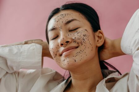 Young woman with glitter face mask relaxing with eyes closed against a pink background, giving a sense of self-care and calm.