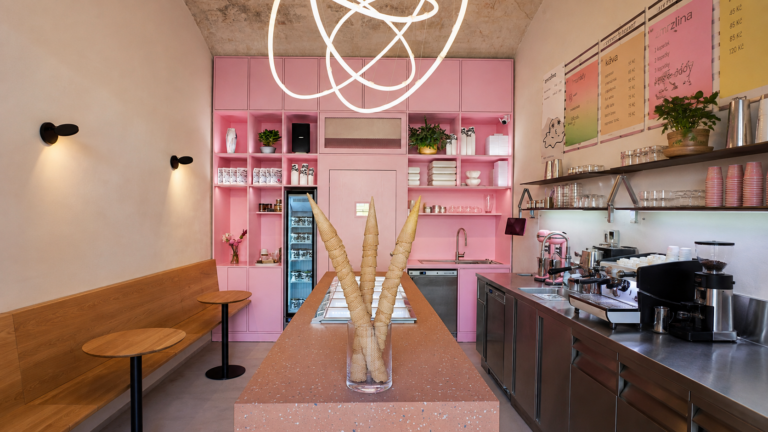 Pink cafe interior with a terrazzo pink counter and three ice-cream-cone sculptures in a glass vase as a centerpiece.