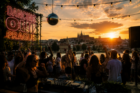 Crowd dancing at a sunset river party near Prague Castle, with a neon sign reading 'DANCING OUT PRAGUE' and a DJ setup in the foreground.