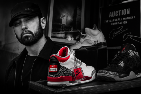 Man in a cap stands beside a display of sneakers; foreground shows a white-and-red Nike sneaker with a red tag, black-and-white background.