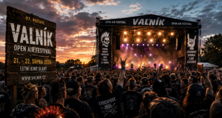 Outdoor stage at Valník Open Air Festival during sunset, with a dense crowd and a large wooden sign reading 'VALNÍK OPEN AIR FESTIVAL' on the left.
