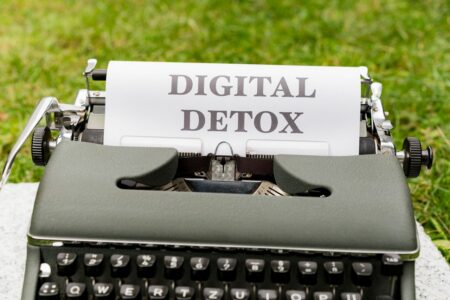 Vintage typewriter with a sheet reading DIGITAL DETOX, set outdoors on grass.