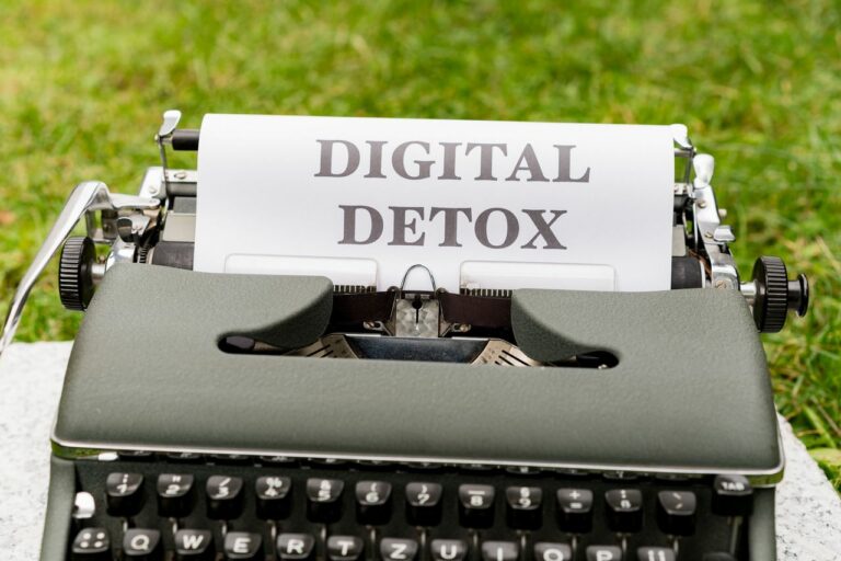 Vintage typewriter with a sheet reading DIGITAL DETOX, set outdoors on grass.